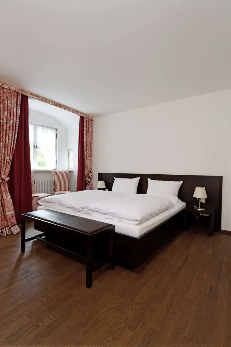 Hotelzimmer mit Doppelbett, Bank und dunklem Holzfußboden