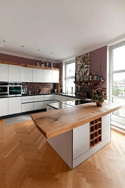 Küche mit weißen Fronten und einem Tresen aus Holz vor Fischgrätparkett